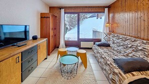 Tunnelmallinen huone, jossa on puusisustus, sohva, televisio ja ikkuna, josta avautuu lumipeitteinen maisema.