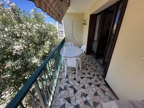 Un balcon doté d’un sol carrelé, d’une table et de chaises blanches, et d’une rambarde verte.