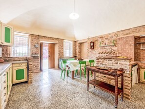 A kitchen with a dining area, featuring a brick wall, green chairs, and a wooden table. - Barba Pipin by Interhome (Penango)