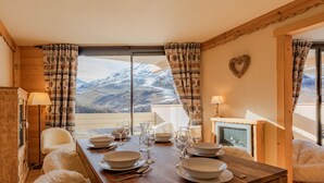 A dining area with a wooden table set for four, a view of snow-capped mountains, and a heart-shaped decoration on the wall. - Cozy chalet with balcony in Belleville (Les Belleville)