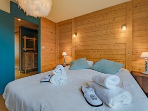 Ett hotellrum med väggar beklädda med träpaneler, en säng med vita sängkläder, två kuddar, ett nattduksbord med en lampa och ett badrum som syns genom en öppen dörr.