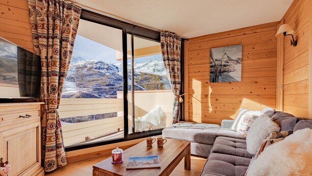 A cozy room with a wooden interior, a sofa, a table, and a view of mountains through large windows. - Cozy chalet with balcony in Belleville (Les Belleville)