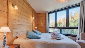 A wooden-paneled room with a bed, two bedside lamps, a window with a view of trees, and a towel on the bed. - Cozy chalet with balcony in Belleville (Les Belleville)