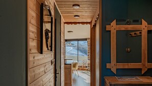 A wooden interior with a wooden door, a window with a view of a snowy landscape, and a wooden cabinet with a picture. - Cozy chalet with balcony in Belleville (Les Belleville)