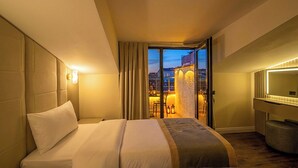 A hotel room with a large bed, a desk, a chair, a mirror, and a view of the city at dusk. - Tumar Istanbul Hotel (Istanbul)