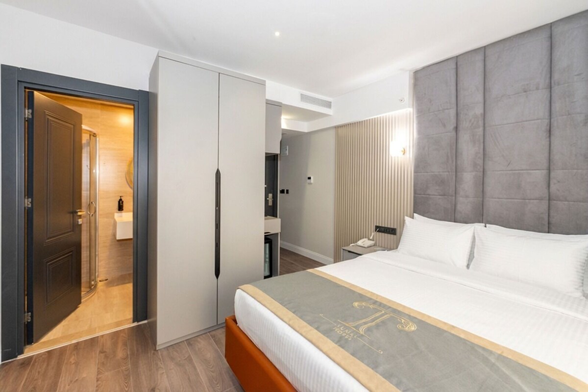 A modern hotel room with a large bed, a wardrobe, and a bathroom visible through an open door.