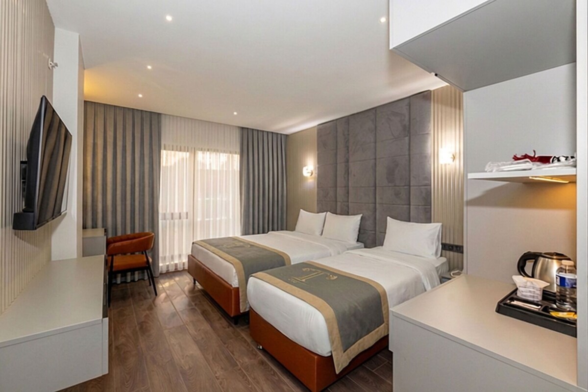 A hotel room with two beds, a desk, a chair, a TV, and a minibar.
