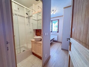 A bathroom with a glass shower enclosure, a wooden vanity with a sink, and a window with a view of buildings. - Beautiful renovated apartment 6 ppl Val Thorens (Val Thorens)