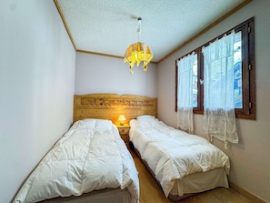 A small, cozy room with two single beds, a wooden headboard with animal carvings, a hanging lamp, and a window with sheer curtains. - Beautiful renovated apartment 6 ppl Val Thorens (Val Thorens)