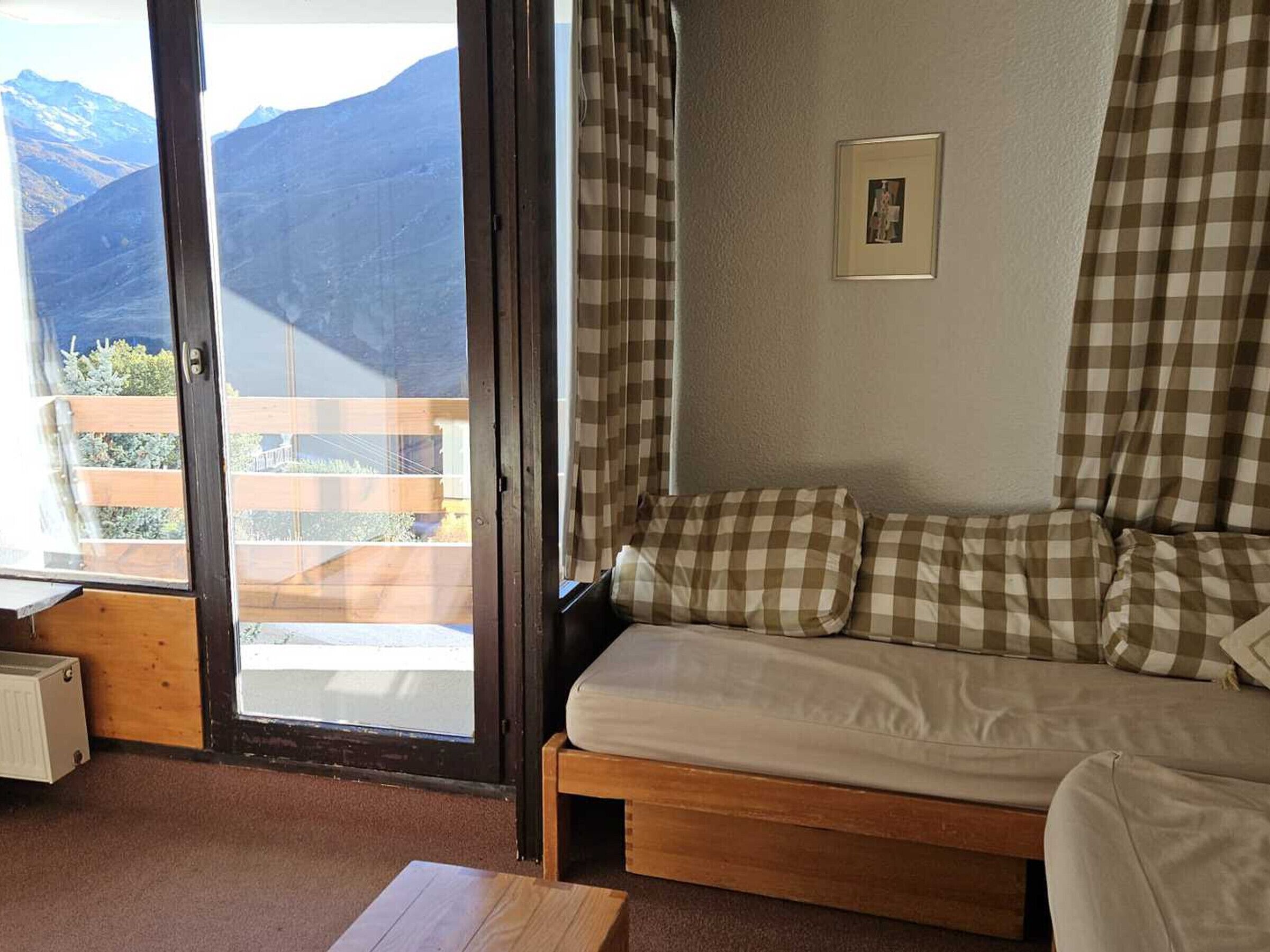 Ein gemütliches Zimmer mit einer Couch, einem kleinen Tisch und Blick auf Berge durch eine Schiebetür.