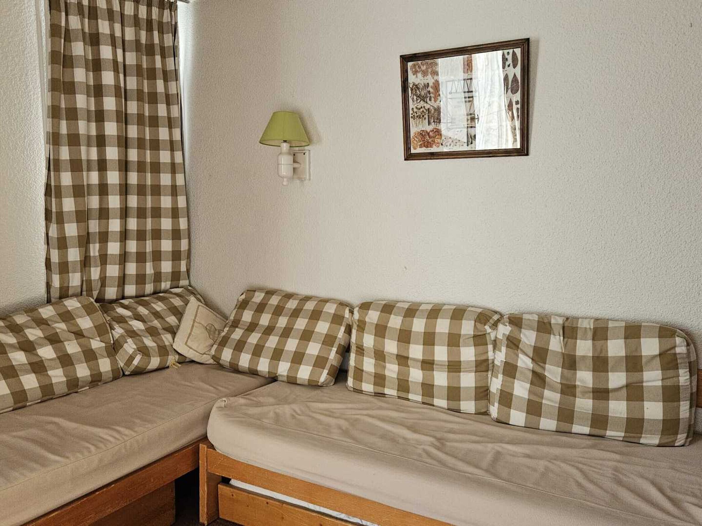 Ein gemütliches Zimmer mit einem karierten Sofa, einer grünen Wandleuchte und einem gerahmten Bild.