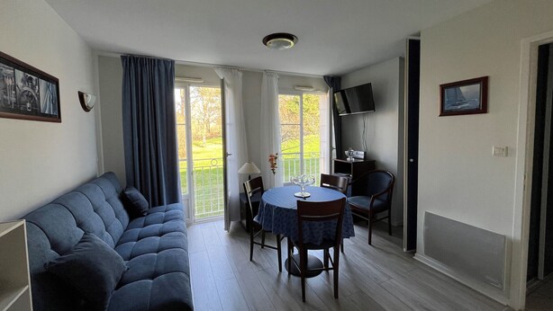 Ein Wohnzimmer mit einer Couch, einem Esstisch mit Stühlen, einem an der Wand befestigten Fernseher und einer Tür, die auf einen Balkon führt.