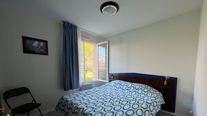 Ein Schlafzimmer mit einem Bett, einem Sessel, einem Fenster mit Vorhängen und einem Bild an der Wand.