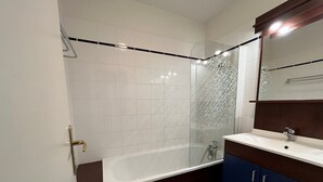 Ein modernes Badezimmer mit Badewanne, Duschkabine aus Glas, weißem Waschbecken und dunkel gehaltenen Schränken.
