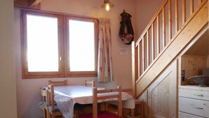 A wooden dining table with six chairs, a staircase, and a window with curtains. - Duplex for 10, near slopes and center (La Plagne Montchavin Les Coches)