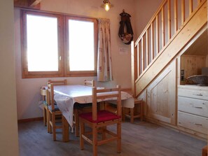 Ein Holzesstisch mit sechs Stühlen, eine Treppe und ein Fenster mit Vorhängen.