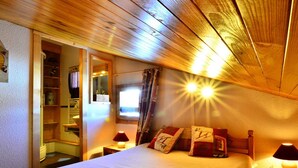 A cozy bedroom with a wooden ceiling, a bed with patterned bedding, two bedside lamps, and a window with curtains. - Duplex for 10, near slopes and center (La Plagne Montchavin Les Coches)