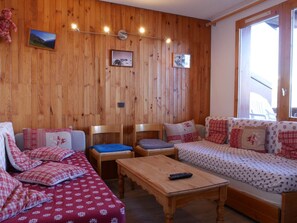 Ein gemütliches Zimmer mit Holzwänden, einer Couch, einem Sessel und einem kleinen Tisch.