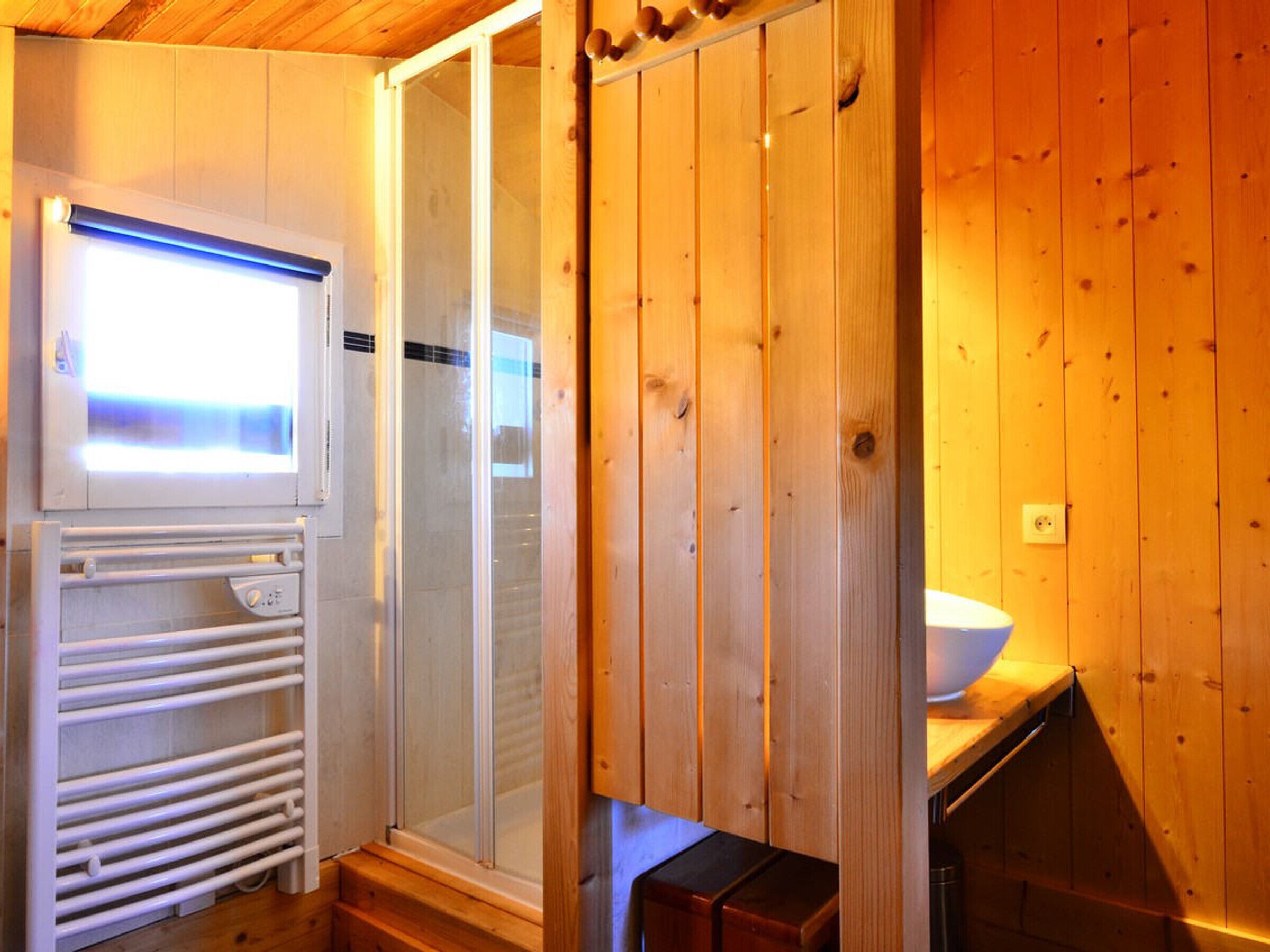 Interior de una cabaña de madera con sauna, ducha envuelta en cristal y un lavabo blanco.