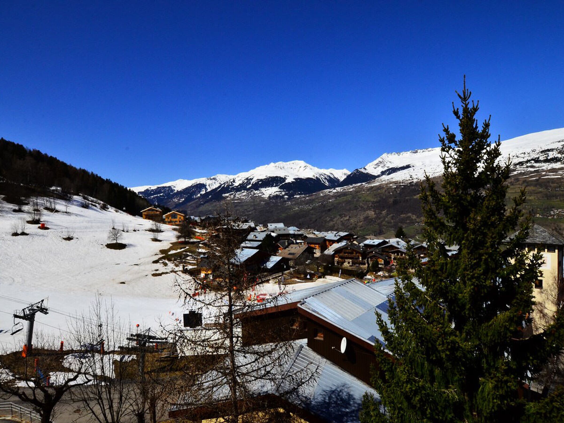 A snow-covered mountain village with wooden buildings and a ski lift in the background.