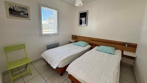 Ein Schlafzimmer mit zwei Betten, einem Heizkörper, einem Fenster, einem grünen Sessel und zwei Bildern an der Wand.