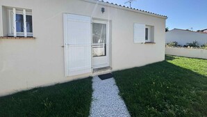 Ein eingeschossiges Gebäude mit weißer Fassade, einem Ziegeldach und einem kleinen Vorgarten mit einem Kiesweg zum Eingang.