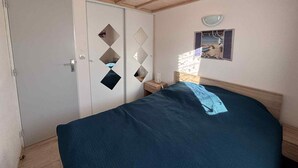 Ein Schlafzimmer mit einem Bett, einem Kleiderschrank, einem Nachttisch und einem wandmontierten Spiegel.
