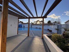 A covered outdoor area with a pool, wooden pergola, and a view of neighboring buildings. - Cottage for 4 people 500m from beach - Terrace and BBQ (La Tranche-sur-Mer)