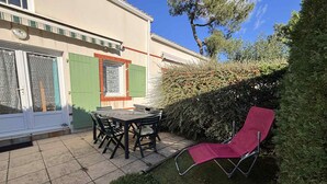 Eine Terrasse mit Tisch und Stühlen, ein roter Klappstuhl und ein Hecken.