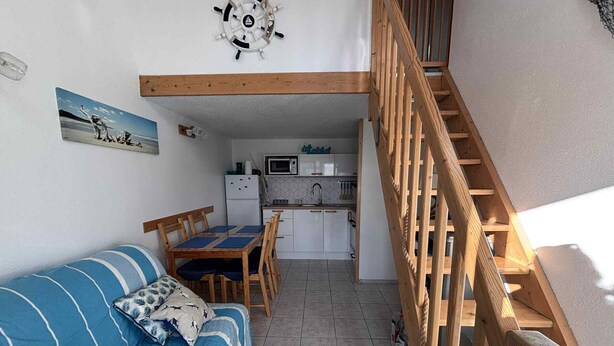 Ein kompakter Wohnraum mit einer Holztreppe, einem Essbereich und einer Küchenzeile.