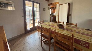 Un comedor con una mesa y sillas de madera, una ventana con cortinas de encaje y vistas a la cocina.