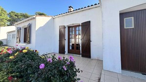Un edificio blanco con un patio empedrado, contraventanas de madera y un pequeño jardín con flores.