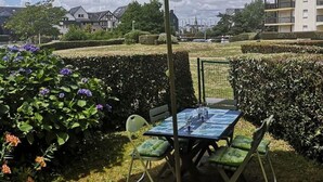 A patio with a table and chairs under a green umbrella, surrounded by hedges and flowering plants. - Renovated T2 apartment, 5 people, pets allowed, Port Crouesty (Arzon)