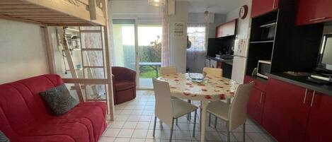 Un espacio habitable compacto con comedor, un sofá rojo, una pequeña cocina y una puerta corrediza que da a un balcón.