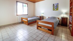 Une pièce avec deux lits en bois, un radiateur, une fenêtre et une bibliothèque.