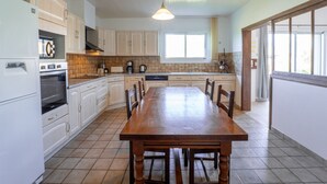 Une cuisine avec des meubles blancs, une table à manger en bois et un luminaire suspendu.