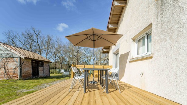 Une terrasse en bois avec une table et des chaises, un parasol et un bâtiment doté d’une fenêtre.