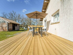 Une terrasse en bois avec une table et des chaises, un parasol et un bâtiment doté d’une fenêtre.