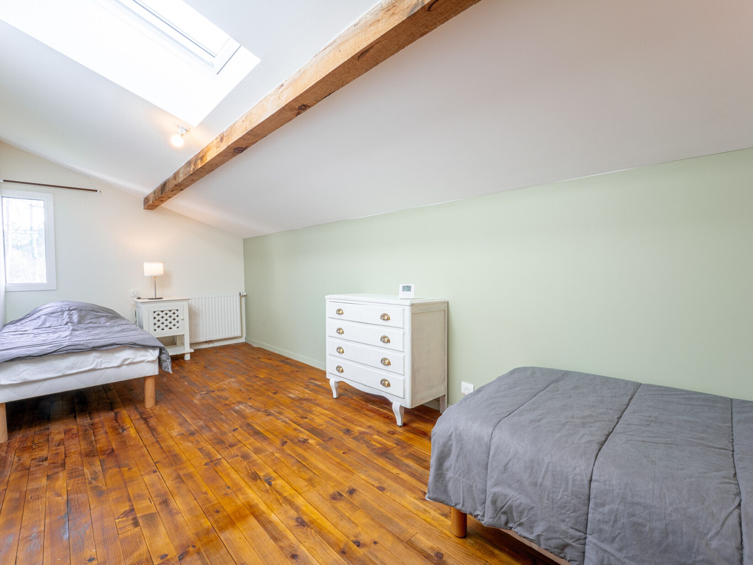 A bedroom with a sloped ceiling, wooden flooring, a bed, a dresser, and a window.