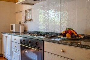 A kitchen with a gas stove, oven, microwave, and a fruit bowl on the counter. - Podere Sant'Eugenio 14, Emma Villas (Chiusdino)