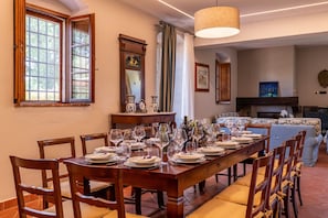 Ein Esszimmer mit einem langen Holztisch, gedeckt für eine Mahlzeit, an dessen Seiten Stühle mit Kissen angeordnet sind.