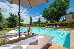 A swimming pool with lounge chairs and umbrellas, surrounded by trees and a brick building. - Podere Sant'Eugenio 14, Emma Villas (Chiusdino)