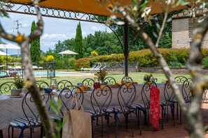 An outdoor dining area with metal chairs and tables, a pool in the background, and a garden with hedges and trees. - Podere Sant'Eugenio 14, Emma Villas (Chiusdino)