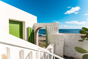 Ein Küstenhaus mit weißer Fassade, grünen Fensterläden und einem Steingewölbe, das zum Meer führt.
