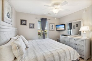 A bedroom with a bed, a dresser, a television, and a ceiling fan. - Grand Beach Resort Condos (Gulf Shores)