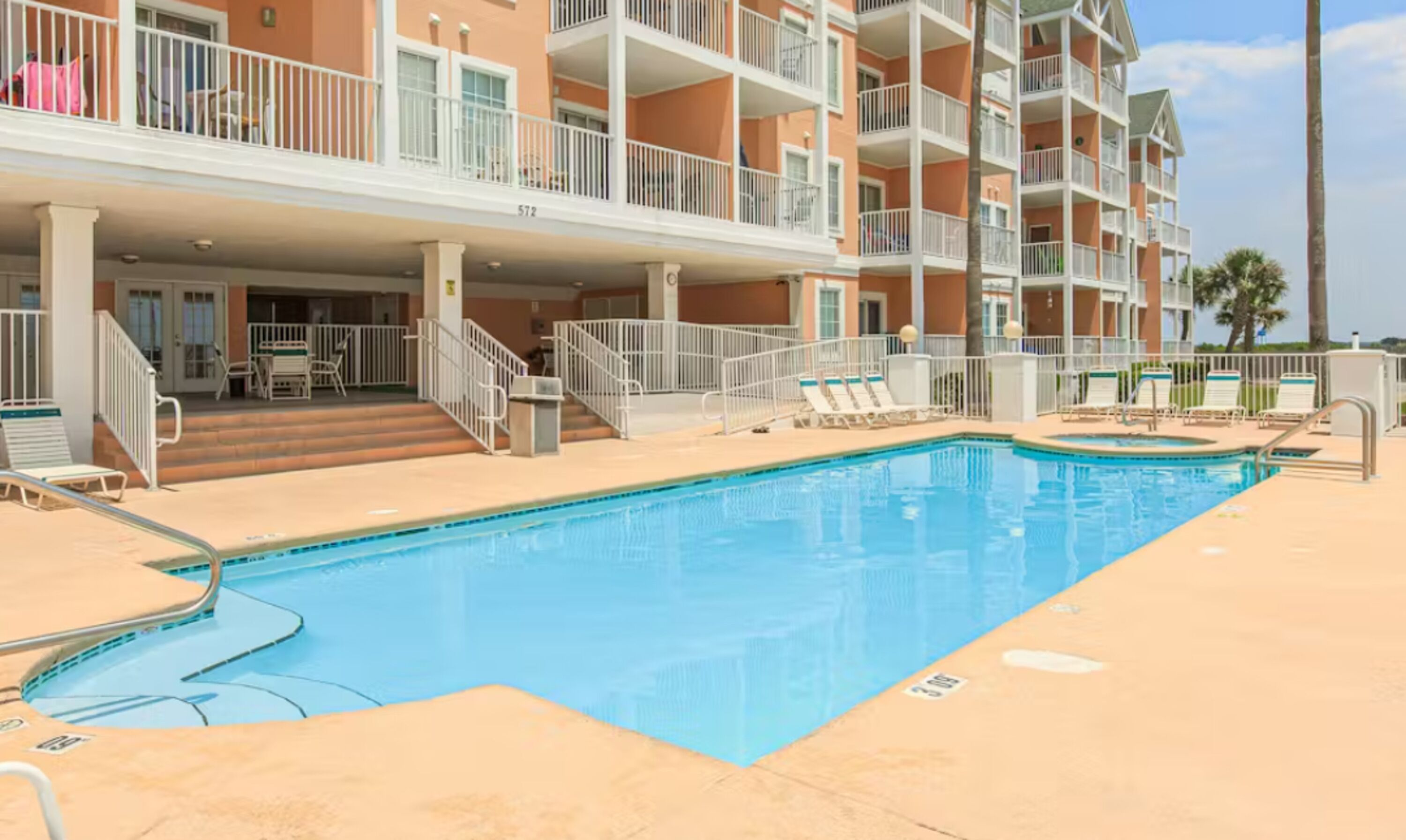 Piscina com espreguiçadeiras e escadaria que leva a um andar superior com varandas.