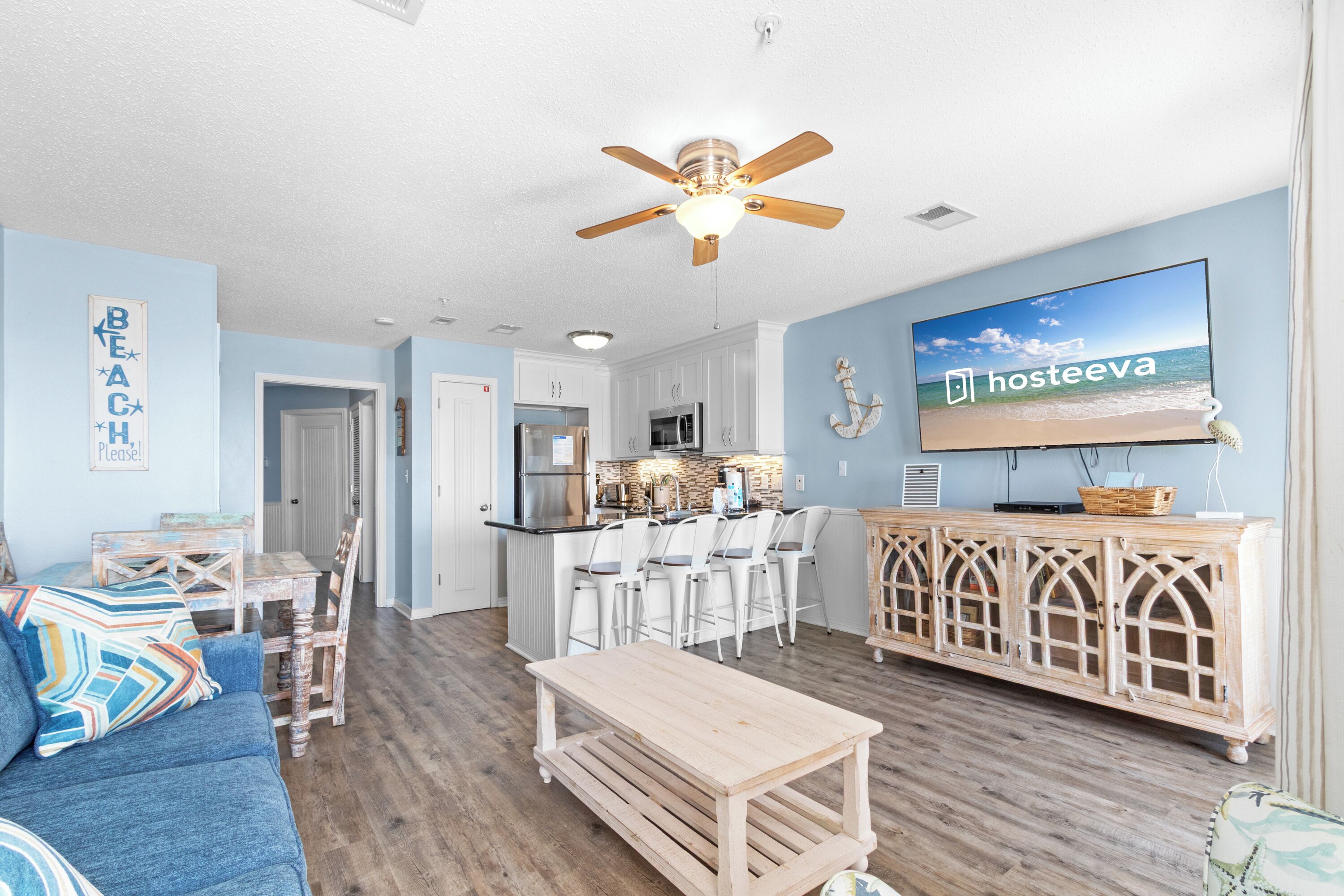 A living room with a blue couch, wooden coffee table, and a TV displaying 'hosteeva'.