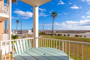 A balcony with a green chair, a white railing, and a view of palm trees and a beach. - Grand Beach Resort Condos (Gulf Shores)