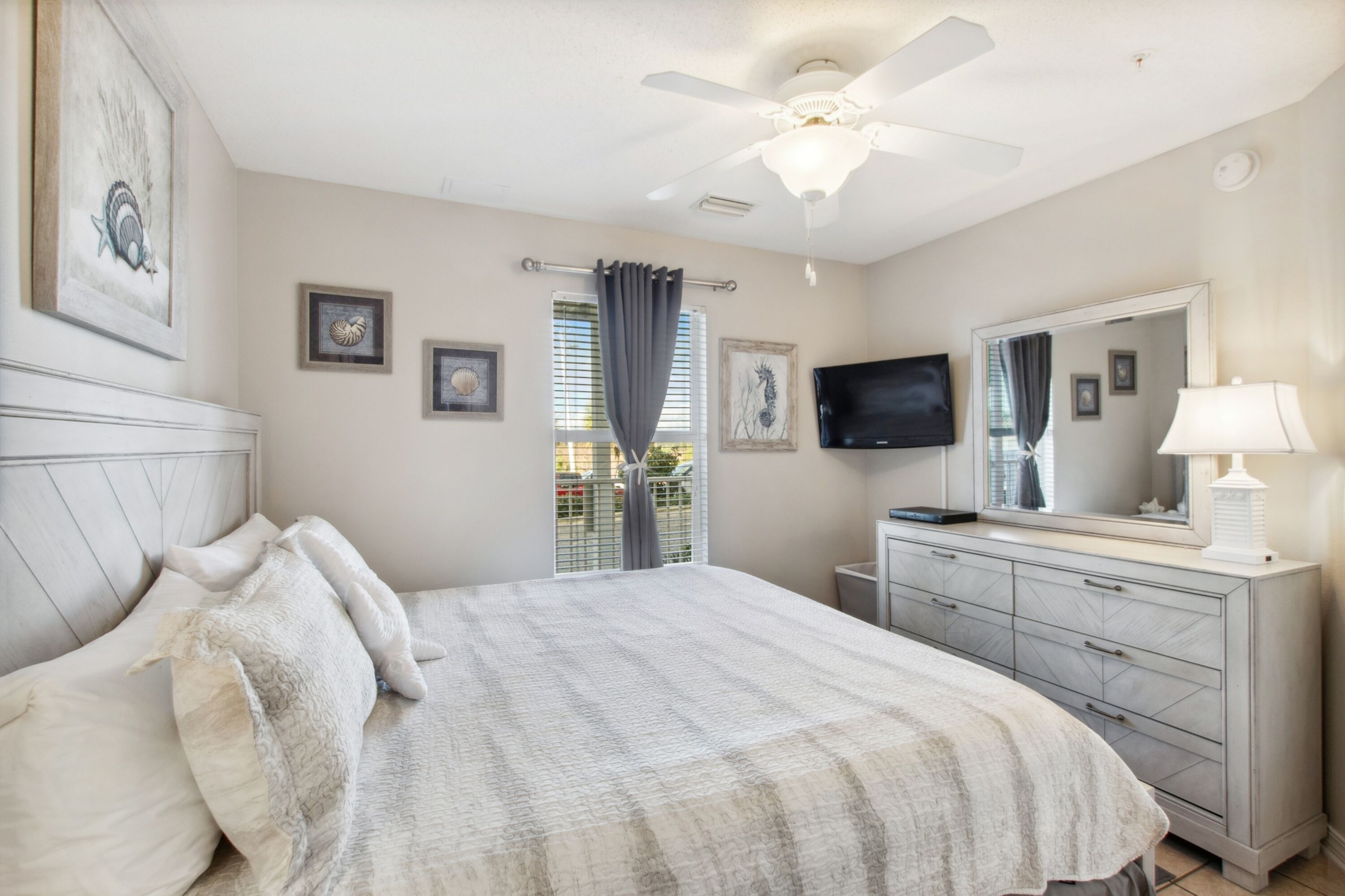 A bedroom with a bed, a dresser, a ceiling fan, a TV, and artwork on the walls.