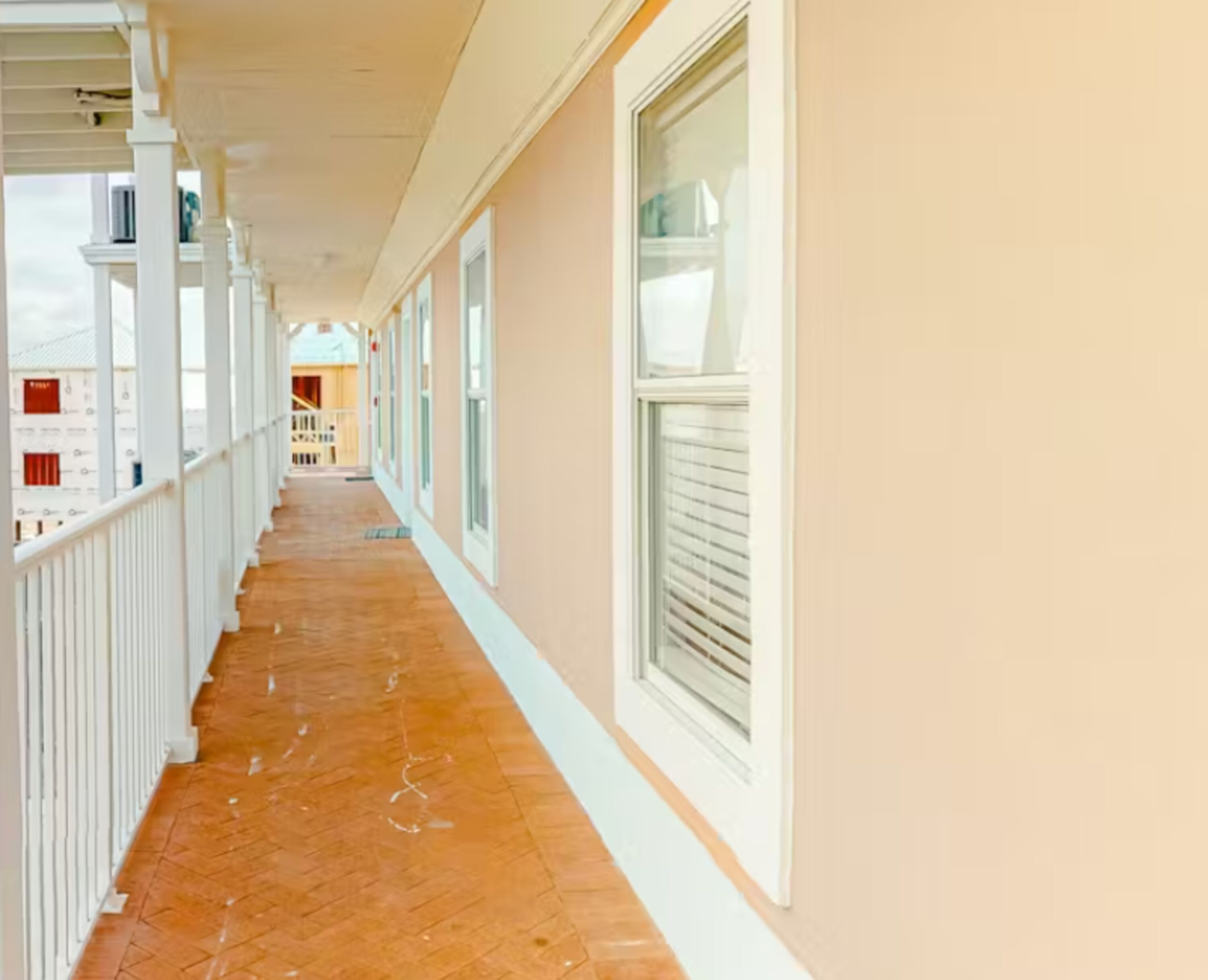 A corridor with a wooden floor, white railings, and windows with blinds.